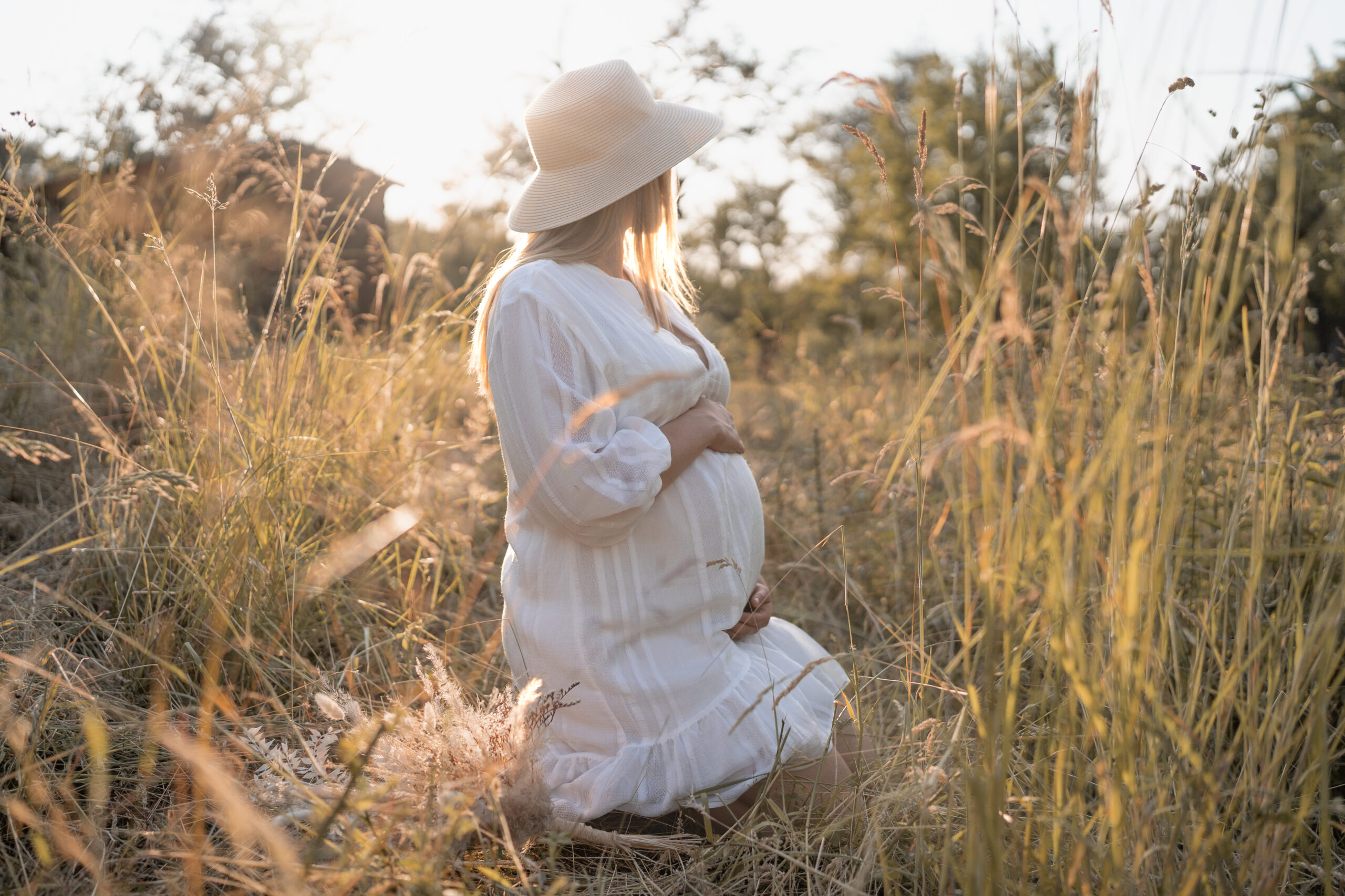 Frau mit Babybauch schaut in den Sonnenuntergang